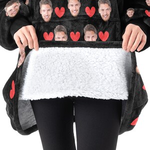 Pu&ograve; includere: Coperta con cappuccio nera con interno bianco e soffice. L'esterno presenta un motivo di cuori rossi e volti. La coperta viene tenuta aperta per mostrare l'interno morbido e bianco. La coperta &egrave; indossata sopra leggings neri.