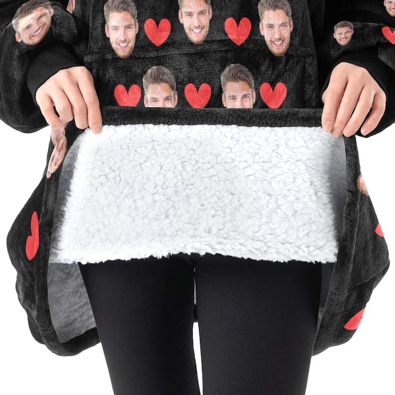 Pu&ograve; includere: Coperta con cappuccio nera con interno bianco e soffice. L'esterno presenta un motivo di cuori rossi e volti. La coperta viene tenuta aperta per mostrare l'interno morbido e bianco. La coperta &egrave; indossata sopra leggings neri.