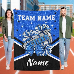 Könnte beinhalten: Eine blau-schwarze Decke mit den Wörtern "TEAM NAME" und "Name" in Weiß. Die Decke zeigt ein Megaphon mit dem Wort "CHEER" und Pompons in Blau und Weiß. Sterne sind über dem blauen Hintergrund verstreut.