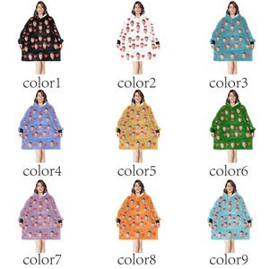 Pu&ograve; includere: Una collezione di coperte con cappuccio in vari colori, ognuna adornata con un motivo di volti e cuori. Le coperte sono esposte su modelli, mostrando le diverse opzioni di colore disponibili, tra cui nero, bianco, blu e arancione. La parola 'color' e un numero sono visibili.