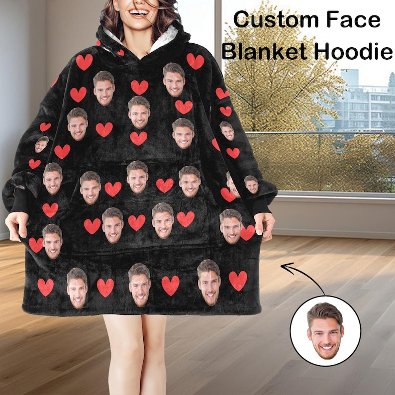 Pu&ograve; includere: Una felpa con cappuccio e coperta nera con un design personalizzato del viso e dettagli a cuore rosso. La felpa con cappuccio ha un'ampia tasca frontale e un cappuccio con interno bianco. Il testo "Custom Face Blanket Hoodie" &egrave; visibile.