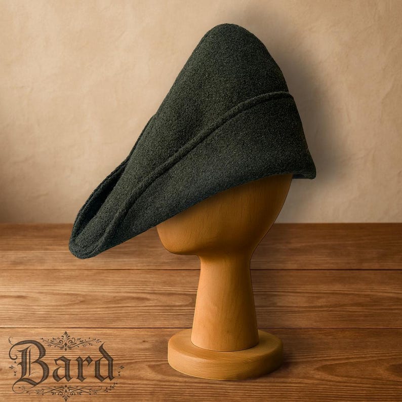 May include: A dark green medieval hat with a pointed crown and a brim, displayed on a wooden hat stand. The hat has a textured appearance and is likely made of wool or a similar fabric. The hat stand is made of light-coloured wood.