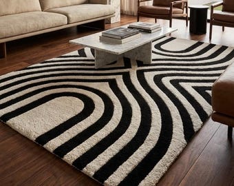 May include: A modern living room featuring a large black and white patterned rug. The rug's design has curved lines. The room also includes a beige sofa, brown leather chairs, a marble coffee table, and a large abstract painting.