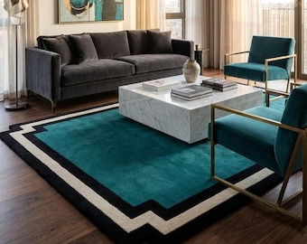 May include: A modern living room featuring a dark gray sofa, teal armchairs with gold frames, and a marble coffee table. A teal rug with black and white geometric borders sits on a hardwood floor. An abstract painting hangs on the wall.