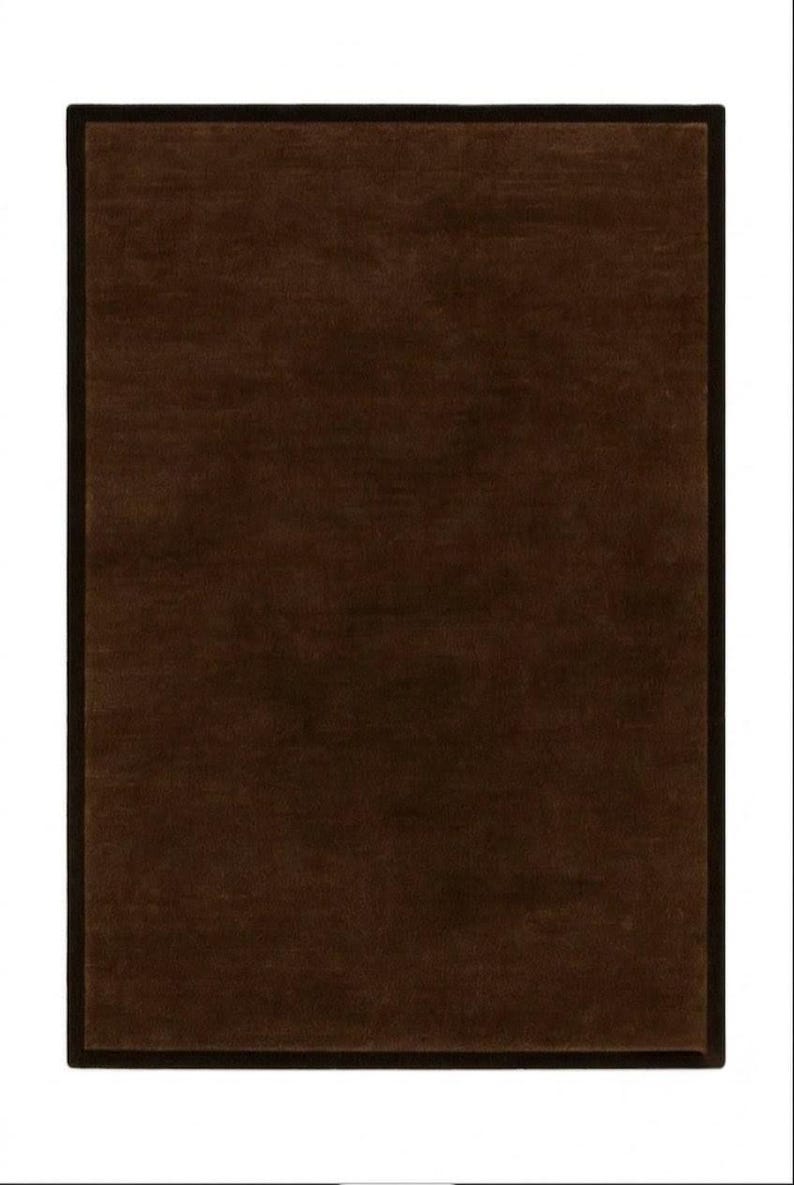 May include: A rectangular area rug featuring a solid dark brown center with a slightly lighter brown tone and a distinct, darker brown border that frames the entire perimeter. The surface appears to have a soft, uniform texture throughout the design.