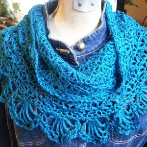 May include: A teal blue crocheted cowl with a lacy design. The cowl is worn on a denim jacket.