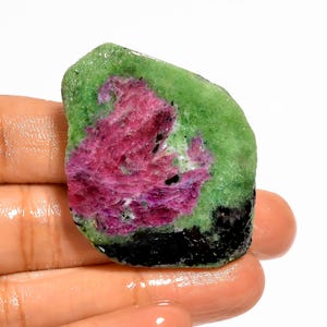 May include: A raw gemstone with a striking colour palette. The stone displays a blend of deep magenta and green, with a black base. The natural, unpolished texture enhances its unique character and appeal.