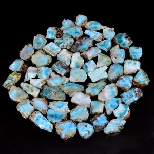 May include: A collection of numerous small, raw Larimar stones arranged in a circular cluster. Each piece displays a unique pattern of sky blue, white, and occasional brown mineral inclusions, with irregular, jagged edges and a natural, unpolished texture.