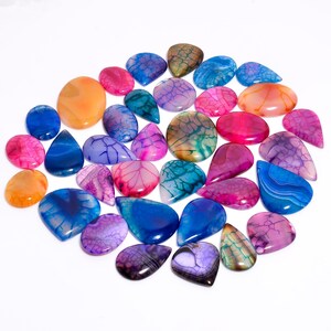 Puede incluir: Una colección de piedras preciosas pulidas de diversas formas y tamaños. Las piedras muestran una gama de colores, incluyendo azul, rosa, naranja, morado y verde, con patrones y vetas únicos. Las piedras preciosas están dispuestas sobre una superficie blanca.