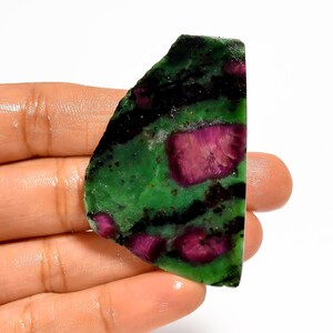 Pode incluir: Uma pedra preciosa polida com uma vibrante mistura de cores. A pedra apresenta uma base de verde escuro, salpicada de preto e pontuada por manchas de vermelho rubi intenso. A forma irregular e as texturas naturais conferem-lhe um apelo bruto e orgânico.