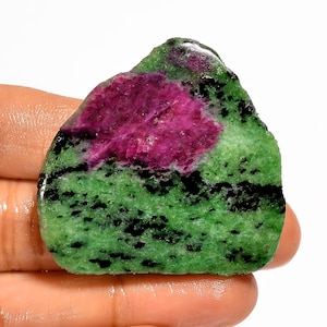 Pode incluir: Uma pedra preciosa em bruto com uma vibrante combinação de cores. A pedra apresenta um centro magenta marcante, rodeado por uma base verde salpicada, com inclusões pretas. A pedra natural é ideal para fazer joias ou colecionar.
