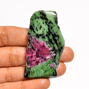 May include: A rough-cut gemstone featuring a vibrant mix of colors. The stone displays a striking combination of green, black, and deep pink hues. The natural, irregular shape of the stone adds to its unique appeal. This gemstone is ideal for jewelry making or collecting.