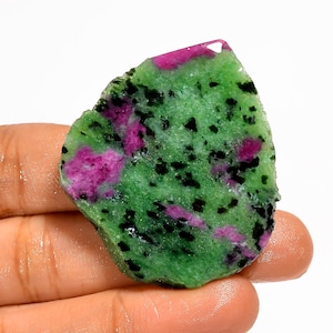 Pode incluir: Uma pedra preciosa em bruto com uma vibrante mistura de cores. A pedra exibe uma base verde com manchas de rosa intenso e salpicos pretos. A forma irregular e a textura natural realçam o seu estado bruto e não polido.
