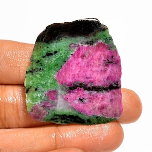 Pode incluir: Uma pedra preciosa em bruto com uma vibrante mistura de cores. A pedra apresenta uma combinação marcante de rosa brilhante, verde profundo e preto. A área rosa é a maior, com áreas verdes e pretas que a delimitam. A pedra é segurada em uma mão.