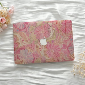 May include: A pink laptop case with a floral pattern featuring large pink flowers, leaves, and other botanical elements. The case has a white Apple logo in the center. The background is a white, textured surface.