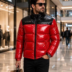 May include: A glossy puffer jacket featuring a vibrant red body and a contrasting black yoke and high collar. The jacket has a full-length black front zipper, horizontal quilted panels, and long sleeves with adjustable cuffs, worn with black pants.