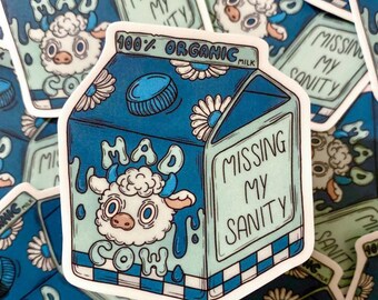 May include: A blue and white sticker featuring a cartoon milk carton with a cow illustration. The text on the carton reads "MAD COW" and "MISSING MY SANITY". The sticker also says "100% ORGANIC MILK".