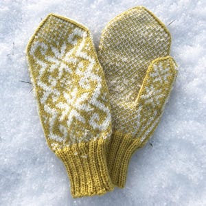 May include: A pair of knitted mittens in a mustard yellow color with white snowflake patterns. The cuffs are a solid mustard yellow, and the mittens are lying on a snowy surface. The mittens are designed for cold weather.