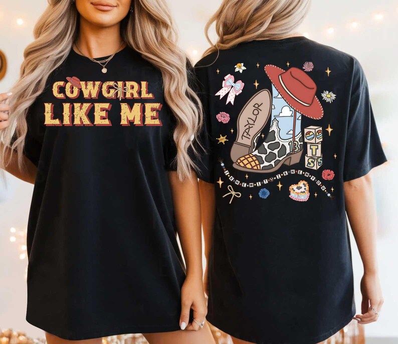 May include: A black t-shirt featuring the text COWGIRL LIKE ME on the front. The back displays a graphic of a cowboy boot with a cow print pattern, a red hat, the name TAYLOR, the number 13, and stacked blocks with the letters T, S, and B.