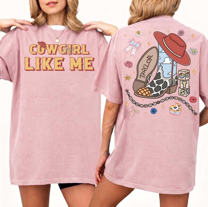 May include: A dusty rose t-shirt featuring the text COWGIRL LIKE ME on the front. The back displays a graphic of a cow-print cowboy boot, a red hat, blocks with the letters T S, and a beaded string with the text I KNEW IT WHEN I KNEW YOU.