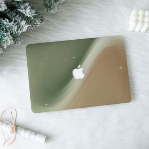 May include: A laptop case with a swirling design in shades of green, beige, and white, featuring the Apple logo. Small white star accents are scattered across the surface. The case is rectangular and appears to be made of a hard, protective material.