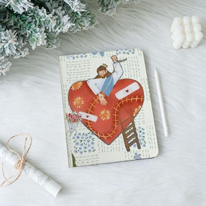 Peut inclure: Un carnet avec une illustration en forme de cœur représentant une figure avec une couronne, des pansements et une échelle. Le cœur est rouge avec des détails cousus. Le fond a un motif floral avec des fleurs bleues.