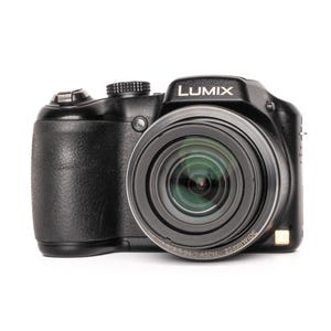 Pode incluir: Câmera digital Lumix preta com uma lente proeminente e o logotipo Lumix na parte superior. A câmera tem uma empunhadura texturizada e vários botões e mostradores. A lente é rotulada como 25mm wide.