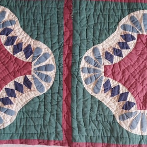 May include: A quilted fabric piece featuring two identical square panels with a dark teal background and a central maroon diamond shape. The design includes light blue petal-like appliqués and dark blue diamond accents on a cream base.