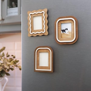 Könnte beinhalten: Drei magnetische Bilderrahmen aus Holz in verschiedenen Formen. Ein Rahmen hat einen gewellten Rand, ein anderer ist rechteckig mit abgerundeten Ecken, und der dritte ist bogenförmig. Ein Rahmen enthält ein Foto einer schwarz-weißen Katze.