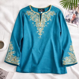 May include: Teal long-sleeve top with gold embroidered floral and paisley designs. The neckline and sleeve cuffs are trimmed with gold. The top has a V-neck and is made of a soft, comfortable material.