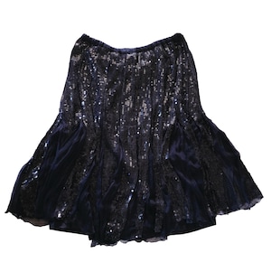 Peut inclure: Jupe bleu marine à sequins avec un ourlet évasé. La jupe présente une taille haute et est composée d'une combinaison de sequins scintillants et d'un tissu plus foncé, semblable à du velours. Idéale pour une occasion festive.