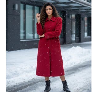 May include: A long, red wool coat with a button-down front and a classic collar. The coat is knee-length and paired with black boots. Snow falls in the background, creating a winter scene.