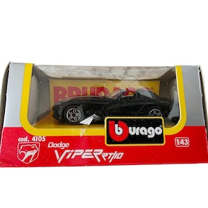 Puede incluir: Un coche de modelo fundido a presión Dodge Viper RT/10 negro en su embalaje original. El modelo se muestra en una caja de plástico transparente dentro de una caja roja, amarilla y plateada. La caja presenta el logotipo de Burago y el nombre del modelo.