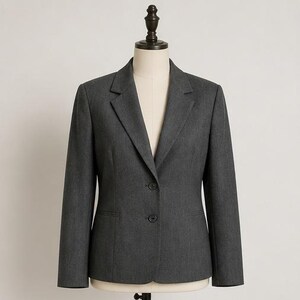 May include: A charcoal gray blazer featuring a notched lapel, long sleeves, and a two-button front closure. The jacket is tailored with structured shoulders and two horizontal welt pockets at the waist, displayed on a mannequin torso.