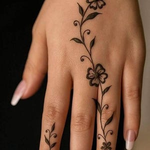 Può includere: Un tatuaggio all'henné marrone scuro con delicati motivi floreali e di viticci che si estendono sul dorso della mano e lungo il dito medio e l'anulare. Il disegno è composto da piccoli fiori a cinque petali, foglie sottili e steli ricurvi.