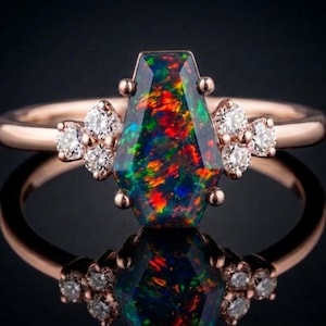 May include: Rose gold ring featuring a large, multi-colored opal gemstone with a unique coffin-like shape. The ring is accented with small, sparkling diamonds on each side of the opal, set against a dark background.
