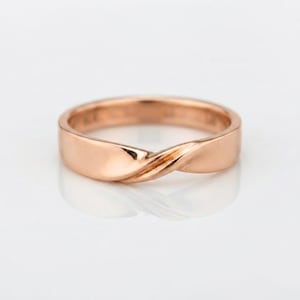 May include: A rose gold ring featuring a smooth, polished band with a central twisted design element. The metal has a warm, pinkish metallic hue and a reflective surface, creating a continuous loop that tapers slightly where the twist occurs.