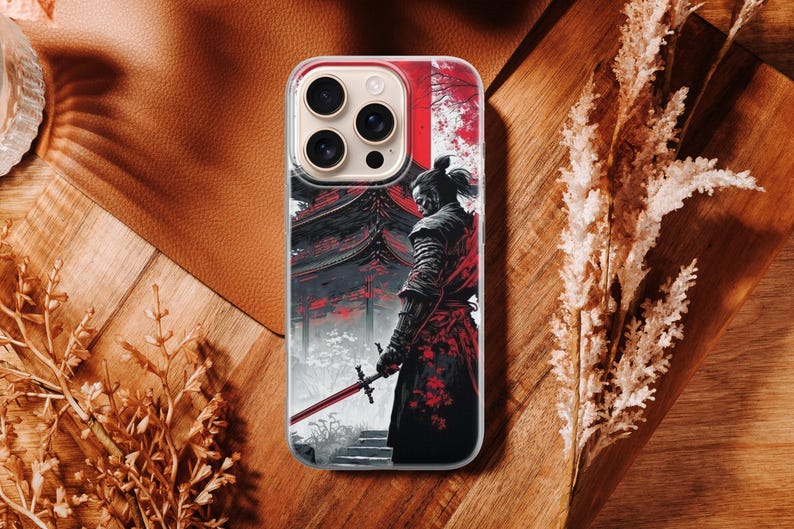 May include: A smartphone case featuring a Japanese samurai warrior with a red and black color scheme. The design includes a traditional building and a warrior holding a sword. The case is on a brown surface.