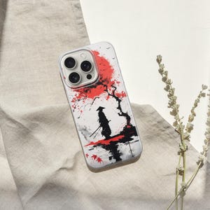 May include: A white phone case featuring a Japanese-style illustration of a samurai warrior standing in front of a red flowering tree. The design is in black, red, and white, with a minimalist aesthetic. The case has a clear border and a camera cutout.