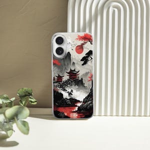 May include: A clear phone case featuring a Japanese landscape design. The artwork depicts red pagodas, a red sun, and a river, set against a backdrop of mountains and trees in shades of black, gray, and red.