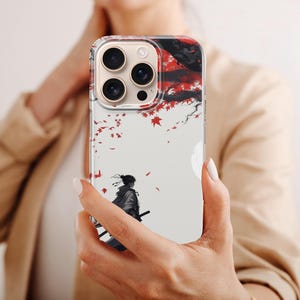 May include: A clear phone case featuring a Japanese-inspired design. The artwork depicts a samurai figure with a sword, set against a backdrop of red leaves and a full moon. The case is designed for a smartphone.