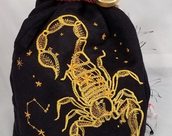 May include: Black velvet drawstring bag with gold embroidered scorpion design, constellation, and zodiac symbol. The bag has a burgundy cord closure and a gold-colored button with a scorpion emblem.