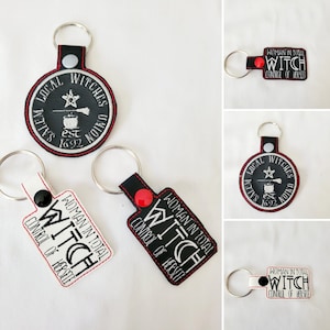 May include: Four different keychains with black and white embroidery. One keychain features a black circle with white embroidery that reads "Salem Local Witches Union Est 1692". The other three keychains are rectangular and feature the text "Woman in Total Control of Herself Witch" in black and white embroidery.