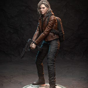 May include: A detailed figurine of a woman in a brown leather jacket, black trousers, and boots, holding a black firearm. She has a backpack and short blonde hair. The figure stands on a circular base with a decorative design.