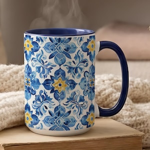 May include: A ceramic mug featuring a repeating blue and yellow watercolor floral tile pattern. The mug has a solid dark blue interior and a matching dark blue handle. The exterior surface displays a symmetrical design of blue petals and yellow centers.
