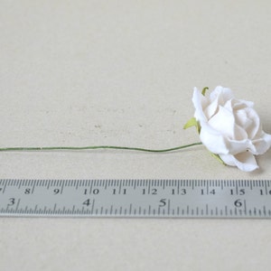 May include: A single white paper rose with a green stem, measured against a ruler.