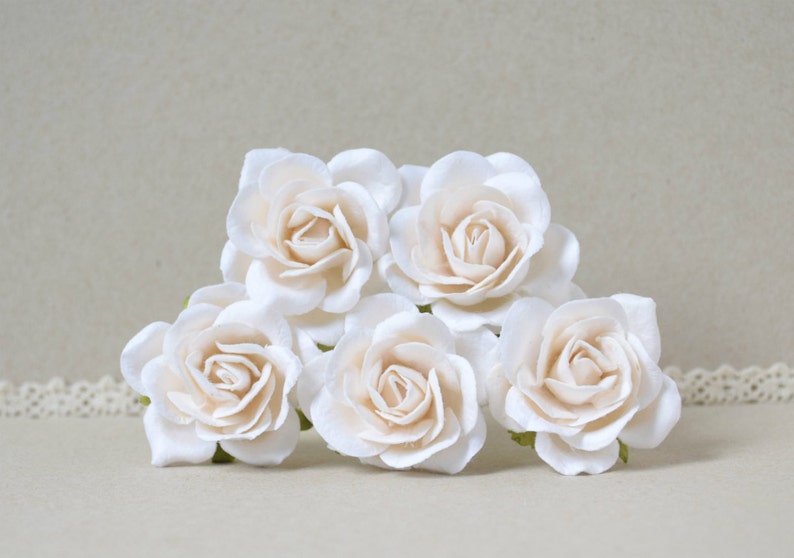 May include: Five white paper roses with a slightly off-white color. The roses are arranged in a cluster, with the center rose slightly higher than the others.
