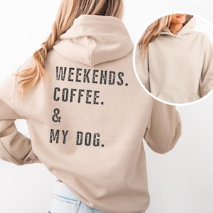 Könnte beinhalten: Beigefarbener Kapuzenpullover mit dem Text "WEEKENDS. COFFEE. & MY DOG." in Schwarz auf dem Rücken. Der Kapuzenpullover hat eine Kapuze und eine Vordertasche. Das Bild zeigt auch eine Nahaufnahme der Kapuze des Kapuzenpullovers.