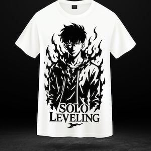 May include: White t-shirt featuring a black graphic of a character from "Solo Leveling" anime. The design includes the character's face and the text "SOLO LEVELING" in bold letters. The character is surrounded by a flame-like design.