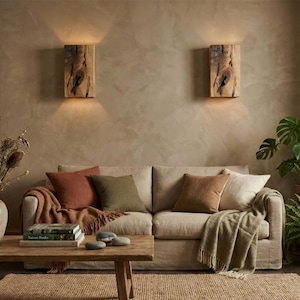 May include: A cozy living room scene with a beige sofa, throw pillows, and a wooden coffee table. Two wooden wall sconces illuminate the space. Plants and a vase of dried flowers add natural elements to the room.